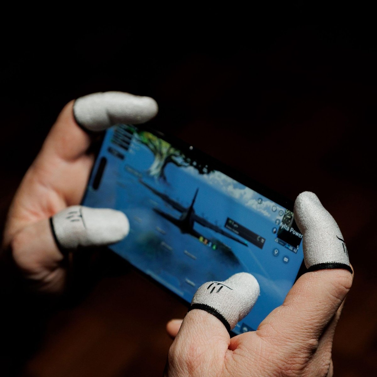 Person holding a smartphone with a game on the screen, wearing white gloves with black accents.