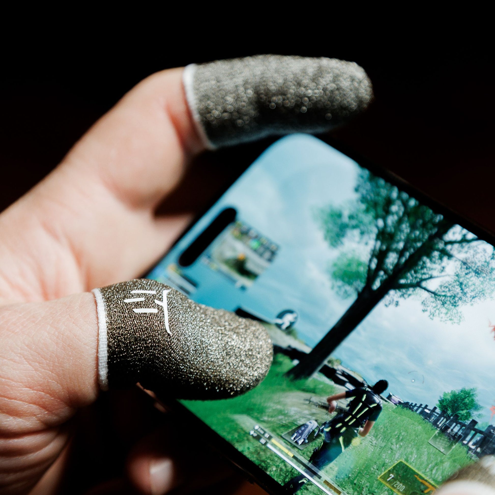 Hand holding a smartphone with a game displayed, wearing two textured finger sleeves.